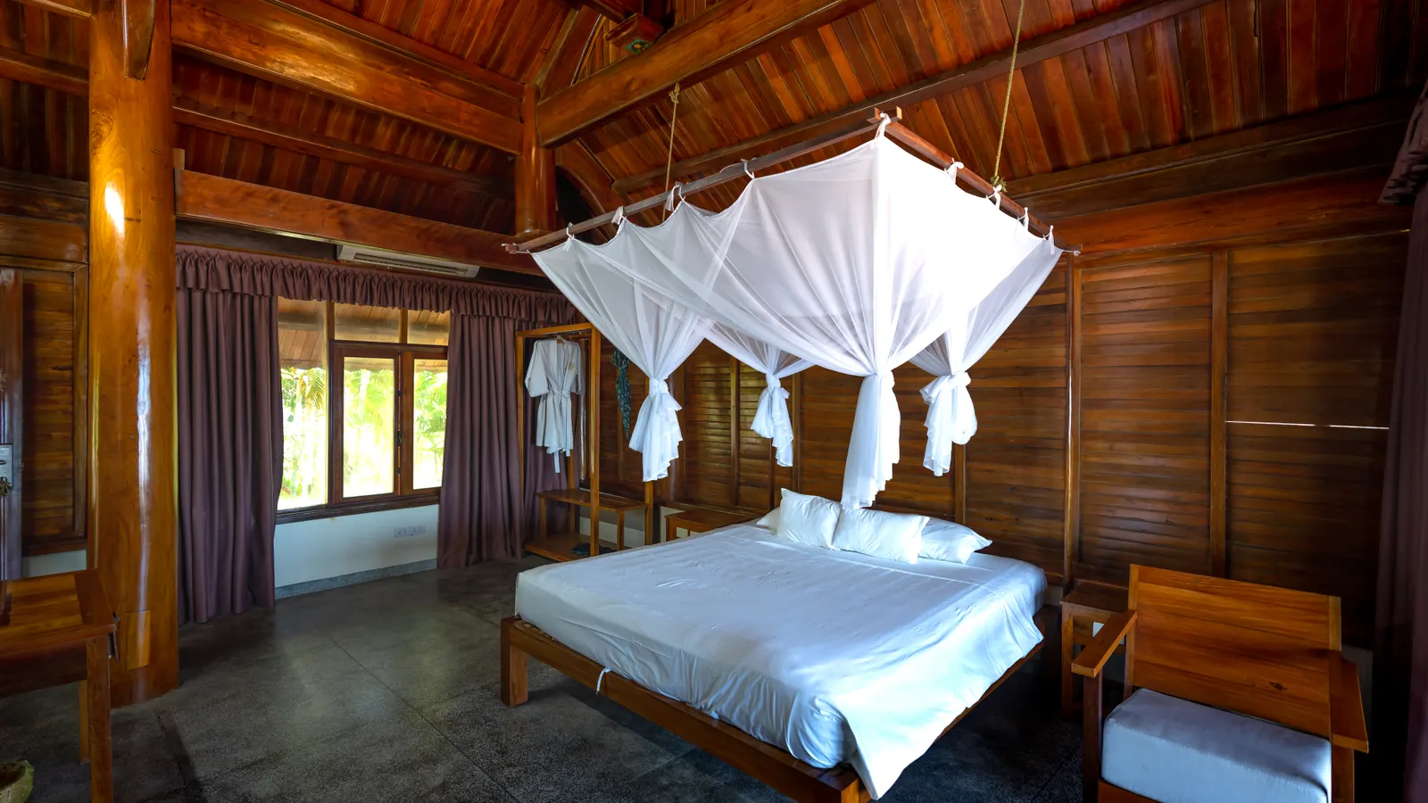A spacious wooden bedroom with a canopy net over the bed